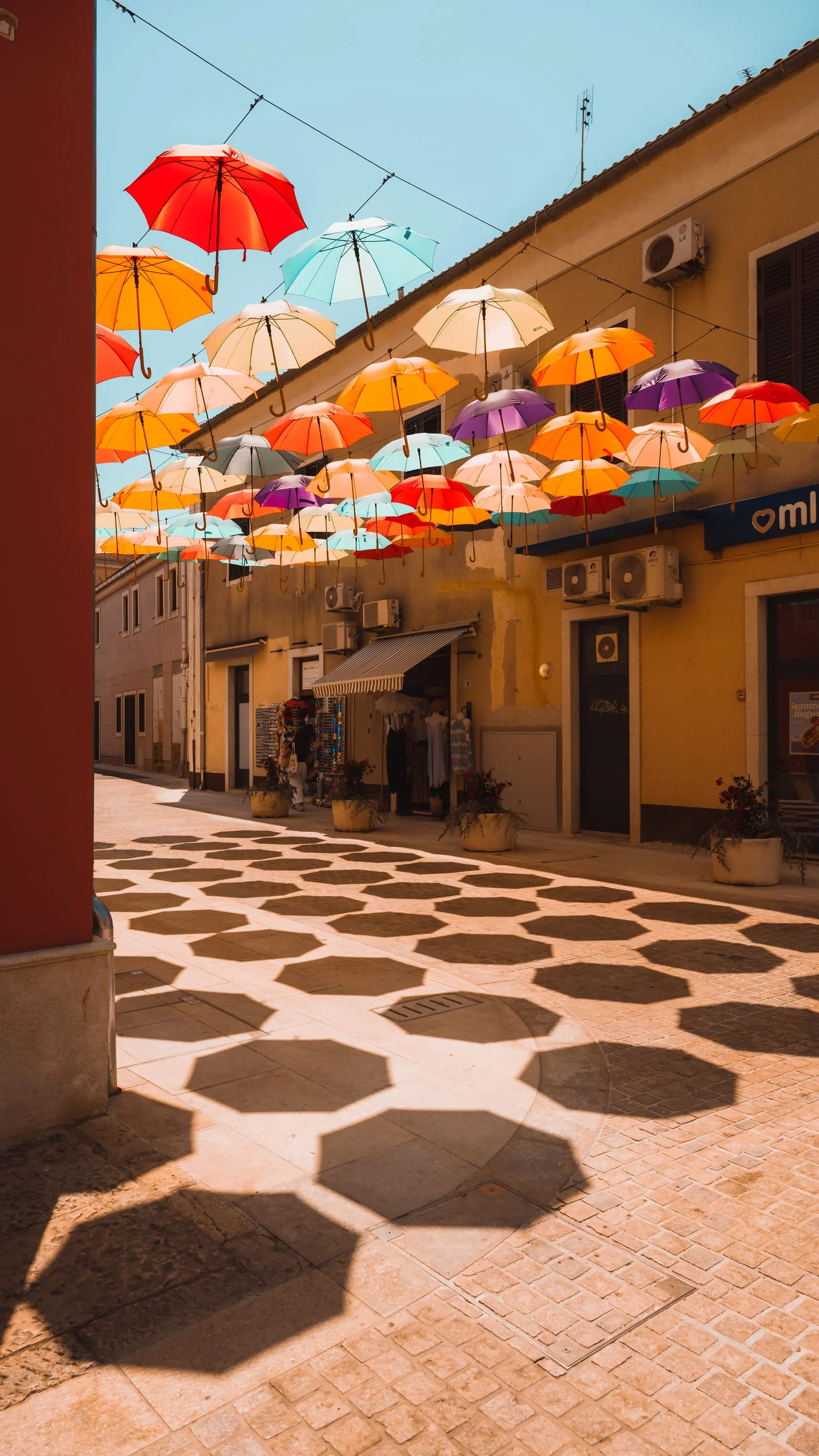Colourful umbrellas above an alley, patterned pavement below