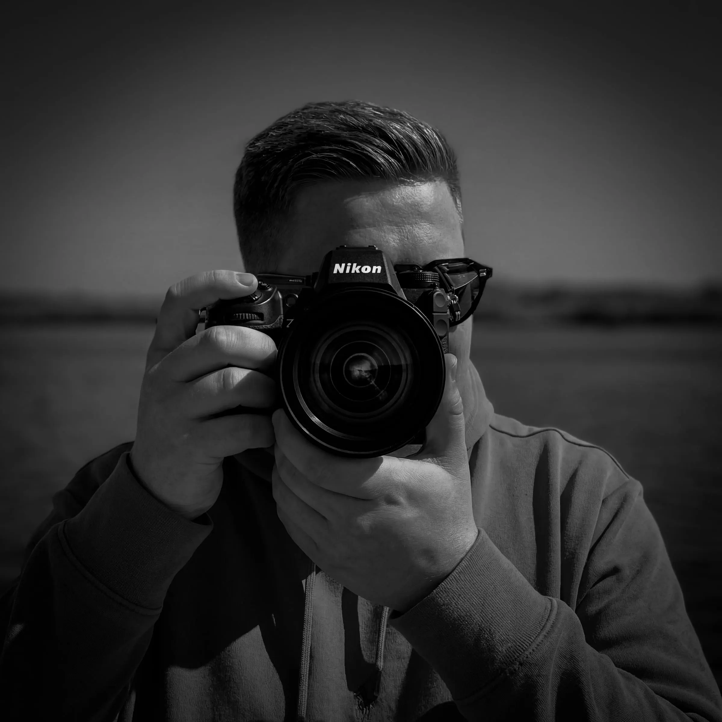 Christopher Gawollek holding a Nikon camera to his face, black and white