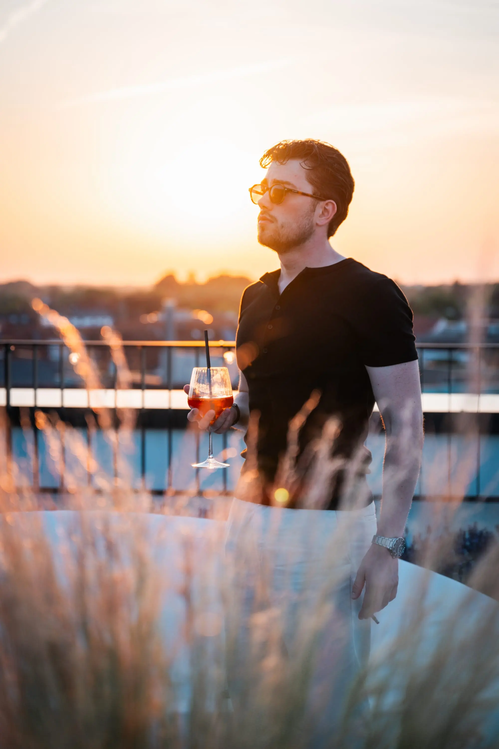 Man with a drink on a rooftop terrace at sunset
