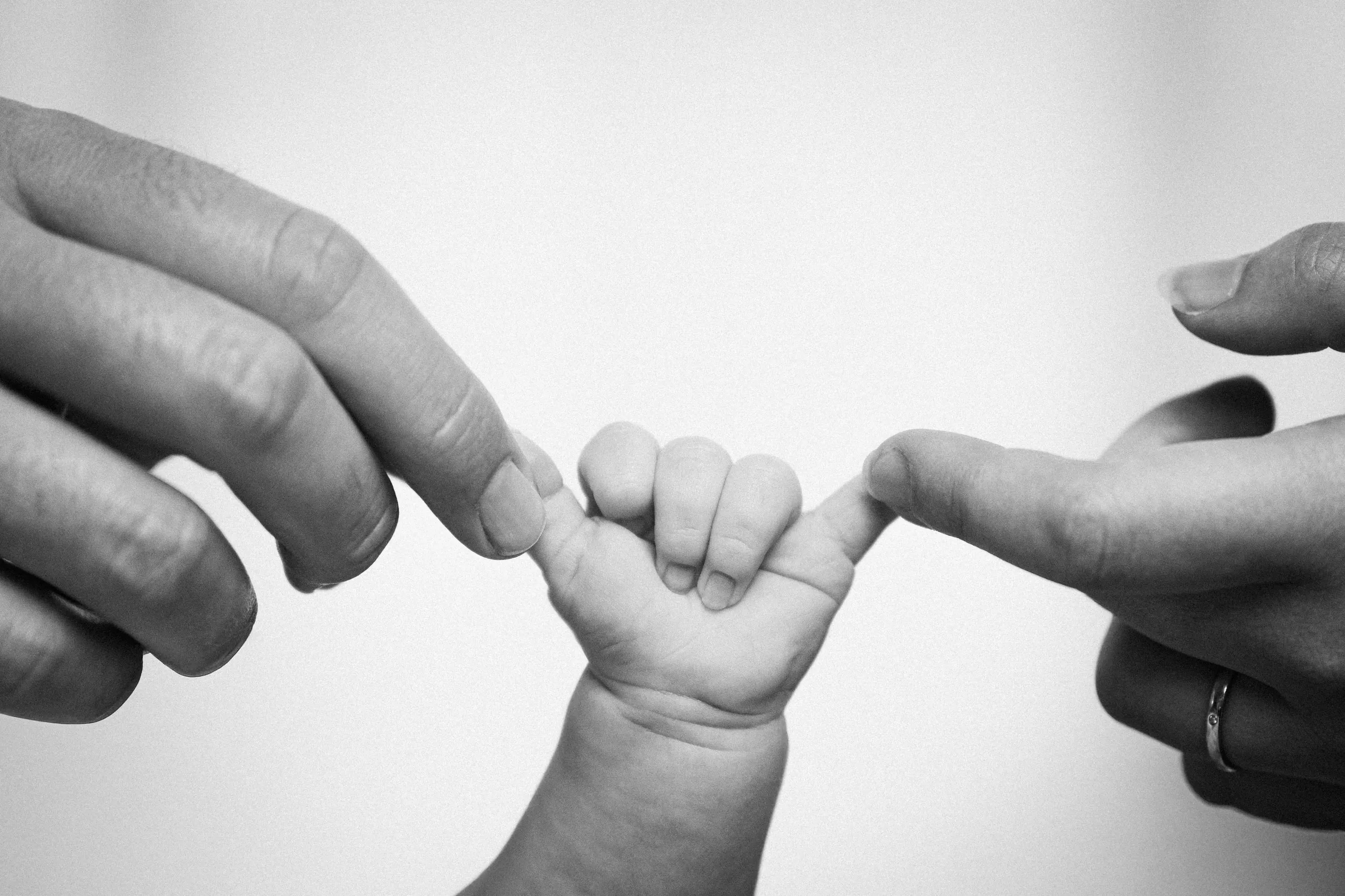 Newborn gripping both parents’ fingers, black and white